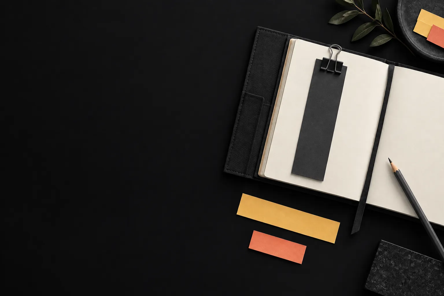 An open day folio with a graphite bookmark and amber and coral strips on a dark surface.